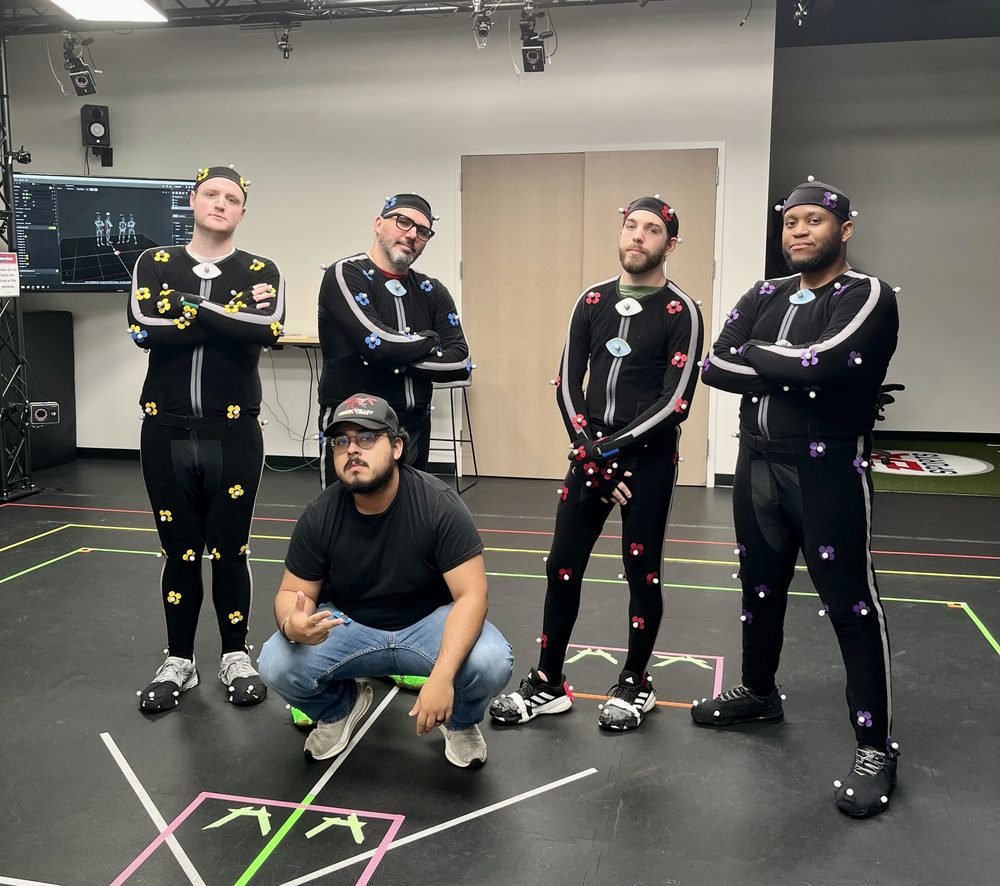 Chris La Croix crouching in front of four colleagues in motion capture suits on a mocap stage
